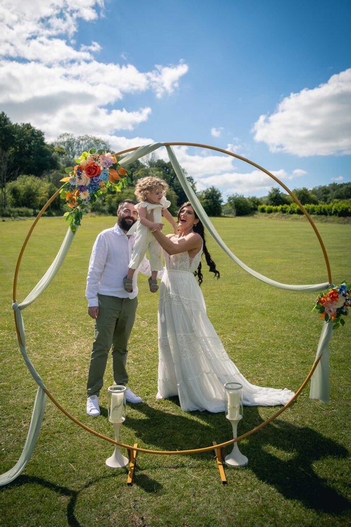 Newly married couple embracing with their baby girl in a beautiful floral circle, symbolizing love, happiness, and new beginnings taken by Professional wedding photographer Hampshire