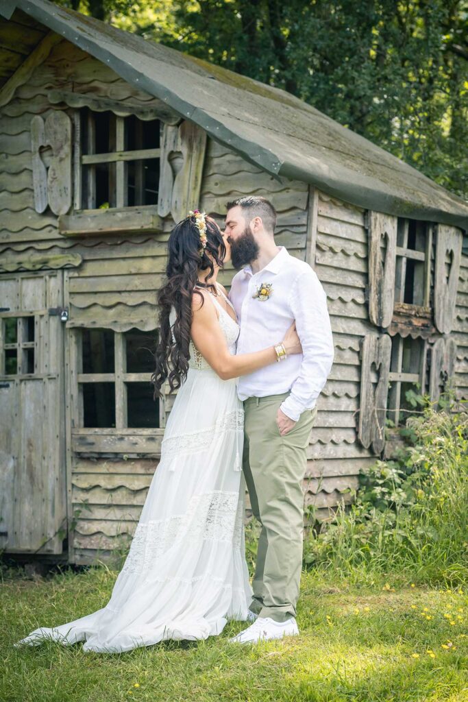 Romantic woodland kiss in Hampshire: bride and groom share a whimsical moment in front of a cosy cottage